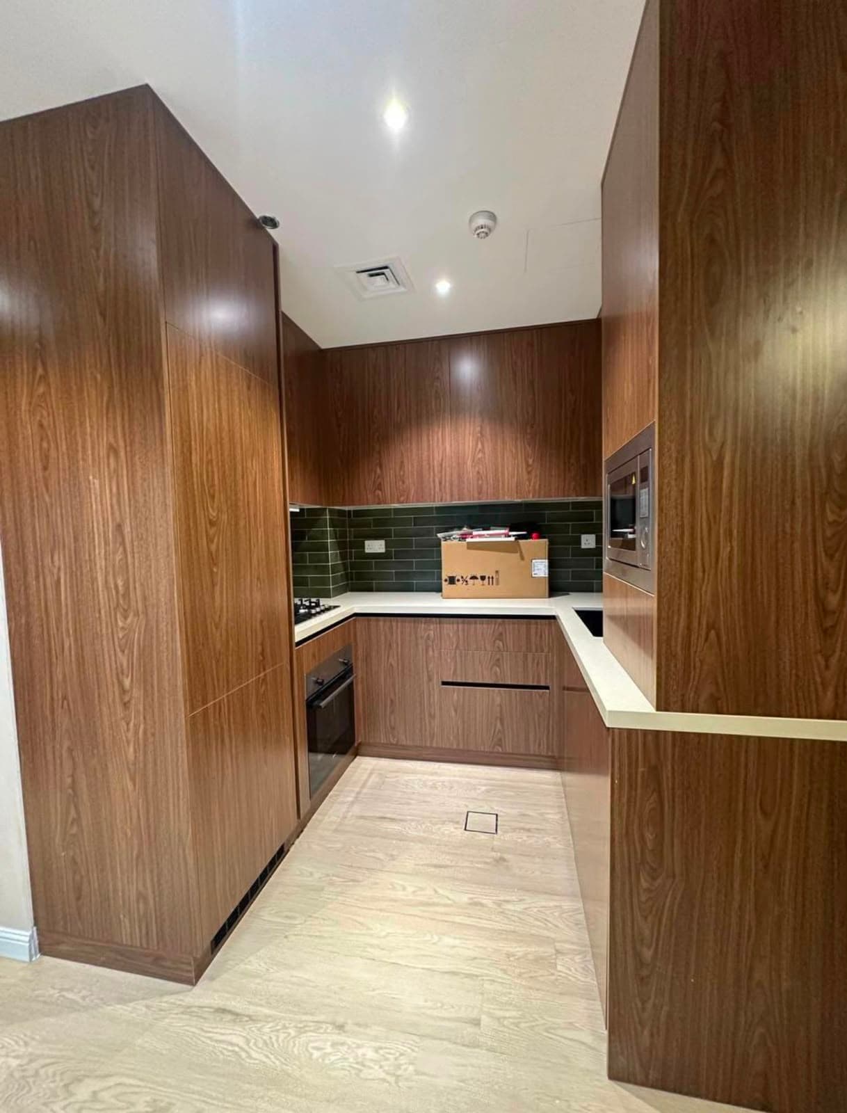 Bespoke walnut kitchen joinery with full-height units, integrated appliances and a green tiled splashback