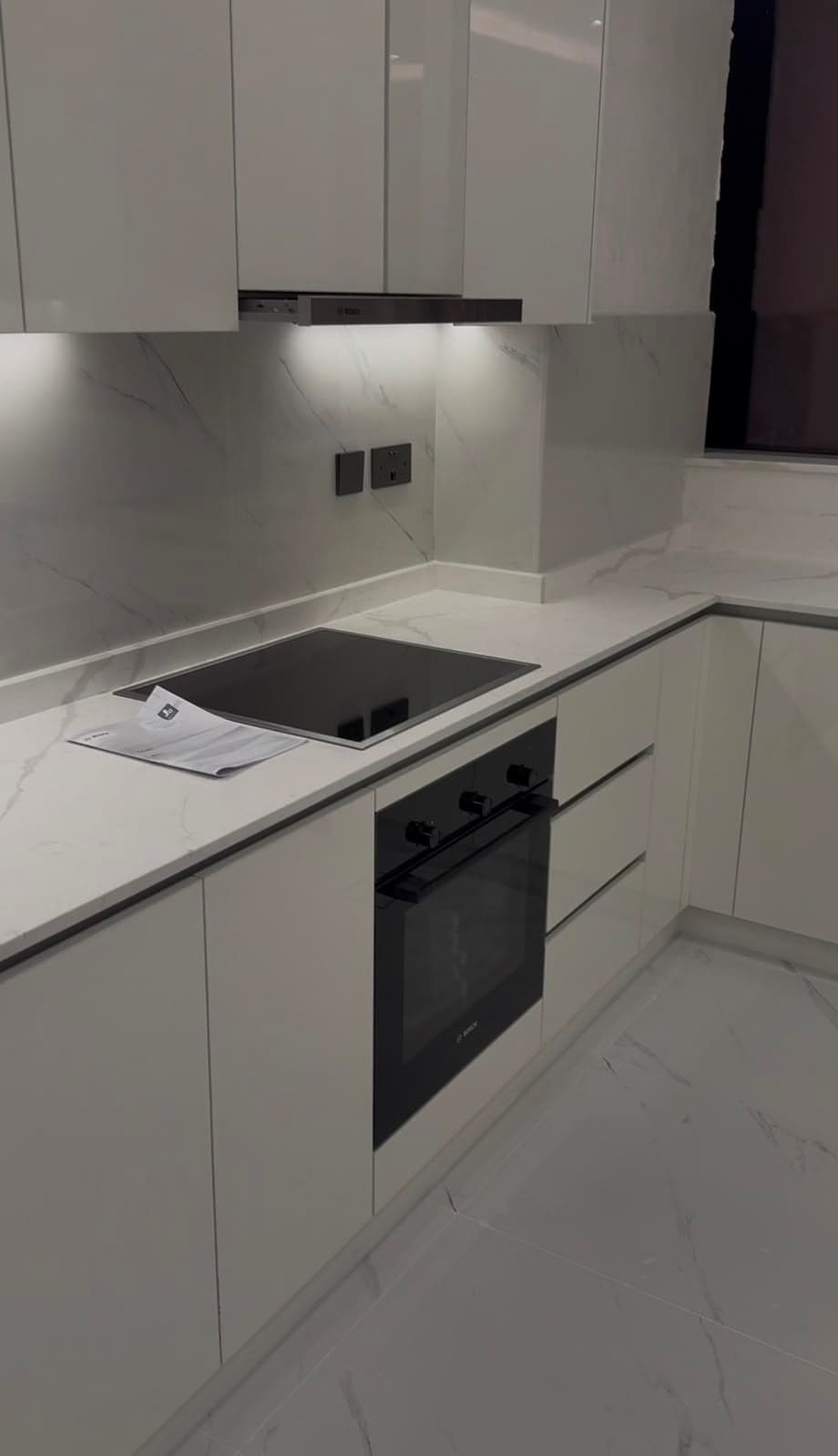 Handleless gloss-white kitchen with a marble-effect splashback, integrated oven and induction hob