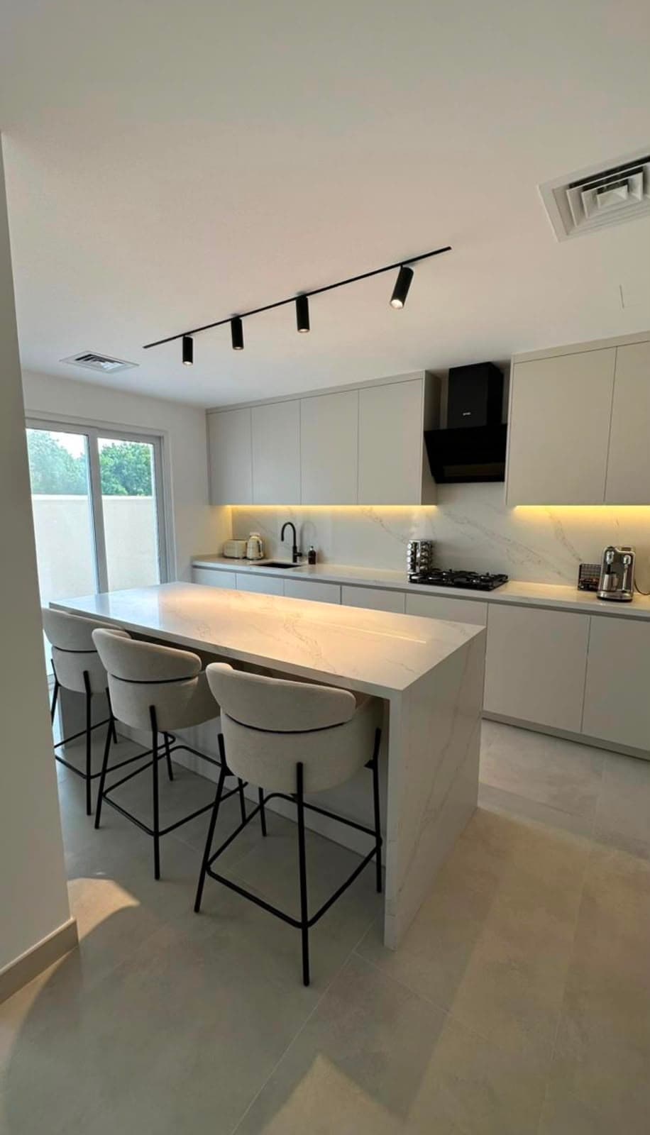 Handleless white kitchen with a marble-effect waterfall island, breakfast bar seating and black track lighting