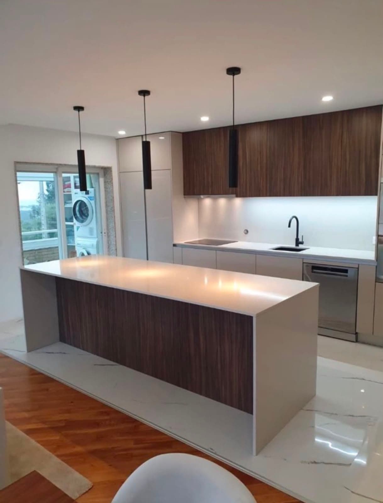 Kitchen island finished in walnut and white quartz with pendant lighting and integrated appliances
