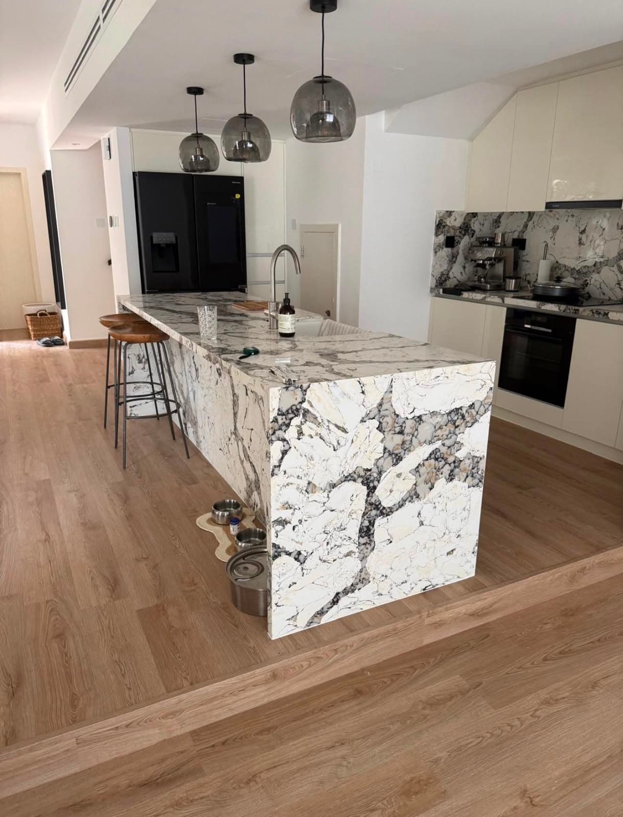 Kitchen with a veined marble waterfall island and wide-plank timber-effect flooring throughout