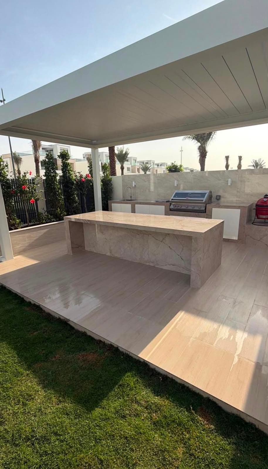 Pergola over an outdoor kitchen with a stone island, built-in barbecue and porcelain-tiled terrace