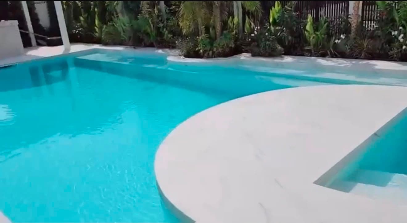 Swimming pool with a curved marble sun-shelf and coping, planting along the boundary behind
