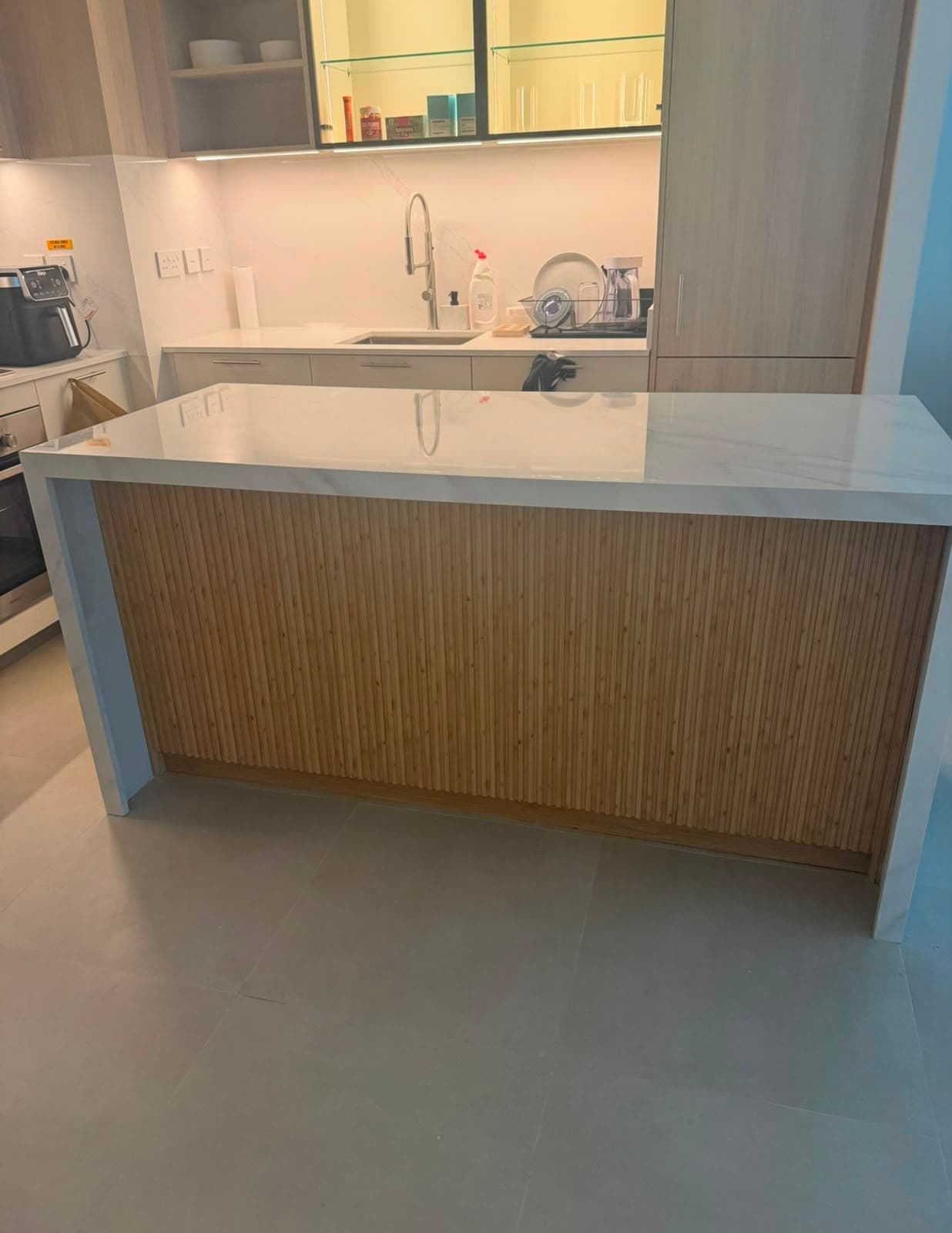 Kitchen island faced in reeded timber with a white quartz worktop and integrated appliances behind