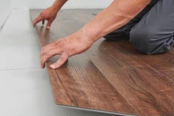 Installer laying a plank of wood-effect SPC flooring onto a prepared subfloor