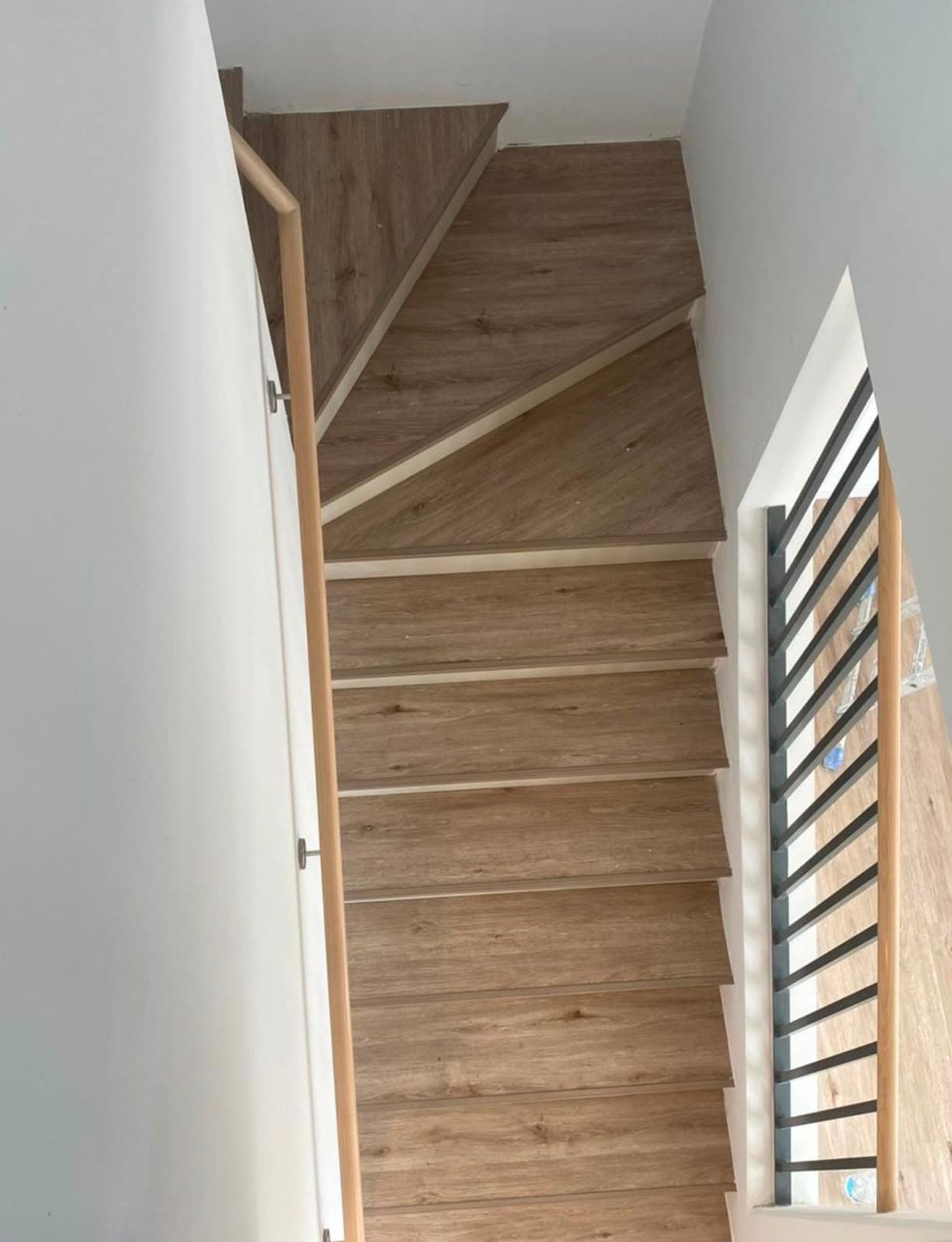 Staircase clad in wood-effect SPC flooring with matching landing and a slatted metal balustrade
